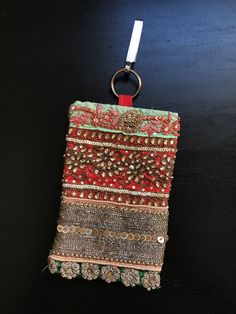 a red and green purse hanging on a black surface with a metal ring attached to it