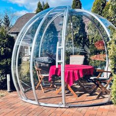 a table and chairs in a large round glass structure on a brick patio surrounded by greenery