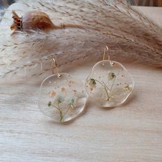 two dandelion earrings sitting on top of a wooden table next to dried grass