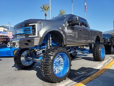 a silver truck with blue wheels parked in a parking lot next to other cars and trucks