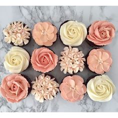 twelve cupcakes decorated with pink and white frosting flowers on a marble surface