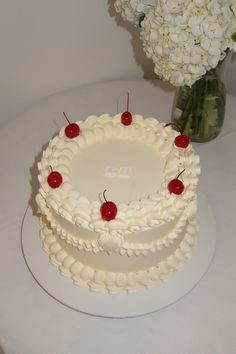 a white cake sitting on top of a table next to a vase filled with flowers