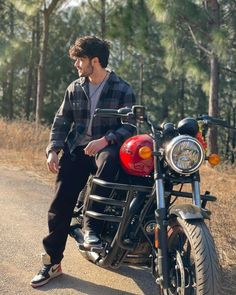 a man sitting on the back of a motorcycle in the middle of the road with trees behind him