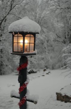 a street light covered in snow with a lit candle on it's side and red garland hanging from the pole