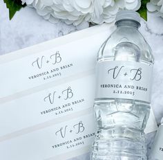 two water bottles with labels on them sitting next to some white flowers and envelopes