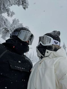 two people standing in the snow wearing ski goggles and jackets with their faces covered by snow