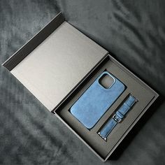 an open box containing a cell phone, watch and wallet on a gray surface with a black background