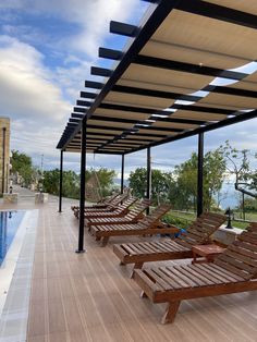 there are many wooden lounge chairs on the deck by the swimming pool with an ocean view