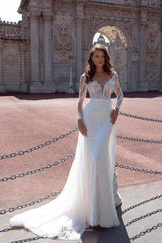 a woman standing in front of a building wearing a long sleeved wedding dress with an open back