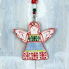 a ceramic angel ornament hanging on a white wooden background with red and green beads