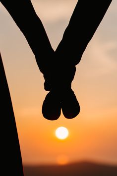 two hands holding each other with the sun setting in the background