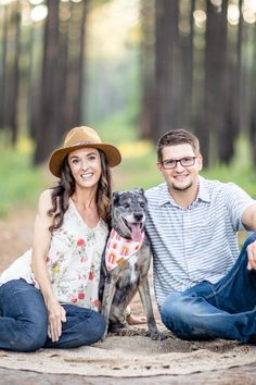 a man and woman are sitting on the ground with their dog in front of them