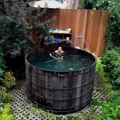 a man is swimming in a large wooden barrel shaped pool surrounded by greenery and shrubbery