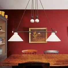 a dining room with red walls and wooden table surrounded by hanging lights, artwork on the wall