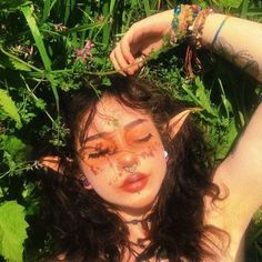 a woman with makeup on her face is laying in the grass and has flowers around her neck