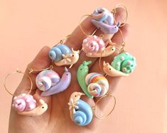 a hand is holding seven small ceramic snails in different colors and sizes, with gold hoop earrings on each ear