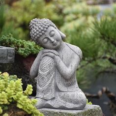 a buddha statue sitting on top of a stone block in front of some plants and rocks