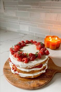 a cake with strawberries on top sitting on a wooden board next to a lit candle