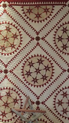 a quilted wall hanging on the side of a red and white wall next to a chair