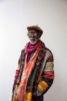 an old man with glasses and a hat is standing in front of a white wall