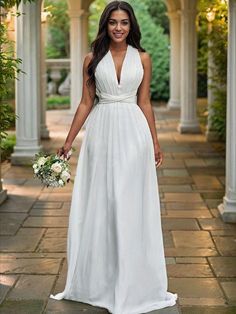 a woman in a white dress standing on a stone walkway holding a bouquet and smiling at the camera