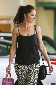 a woman walking down the street with shopping bags in her hand and wearing black tank top