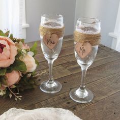 two wine glasses sitting on top of a wooden table next to a bouquet of flowers