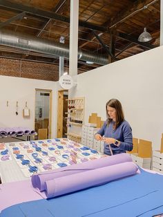 a woman standing in front of a table covered with purple and blue paper, surrounded by stacks of cardboard boxes