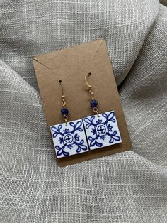 a pair of earrings with blue and white designs on them sitting on a piece of fabric