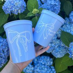 two people holding up blue cups with flowers in the background