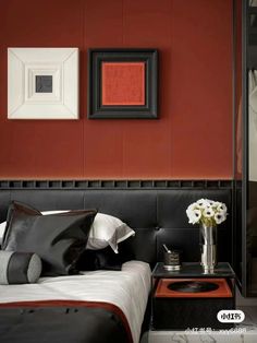 a bedroom with red walls and black bedding is pictured in this image, there are two framed pictures on the wall above the bed