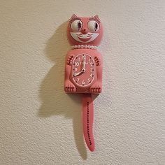 a pink clock with a cat face on it's face is hanging from the wall