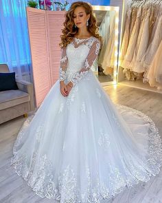 a woman standing in front of a white wedding dress with long sleeves and lace detailing