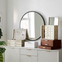 a dresser with drawers and a round mirror on the wall above it is filled with jewelry boxes