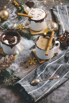 two mugs filled with hot chocolate sitting on top of a table next to christmas decorations