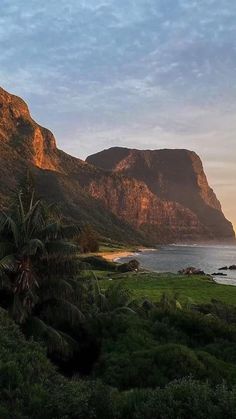 the mountains are next to the ocean and trees on the grass near the water's edge