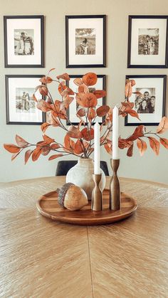 a wooden table topped with two vases filled with flowers and candles next to pictures on the wall