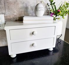 a white dresser with flowers and an egg on top that says messess next to it