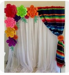 colorful paper flowers are hanging on the wall next to a drape with white curtains