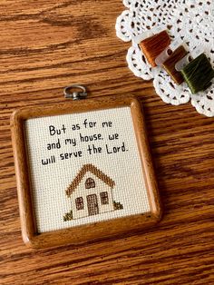 a wooden frame with a cross stitch pattern on it and a tiny house keychain