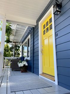 a yellow door on the side of a blue house next to a gray and white porch