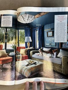 an open magazine with pictures of living room furniture and decor on the pages, in front of a person's hand