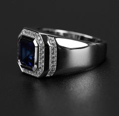 an engagement ring with a blue stone surrounded by white diamonds on a black table top