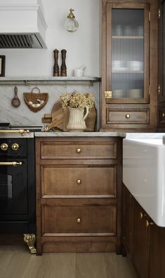 a kitchen with wooden cabinets and marble counter tops, black stove top oven and white sink