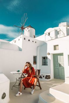 a woman sitting on a chair in front of a building with a windmill behind her