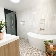 a large white bath tub sitting next to a wooden stool in a bathroom under a light fixture