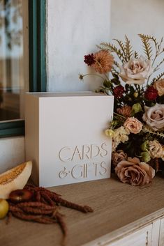 a card and flowers on a table next to a box with cards and gifts written on it