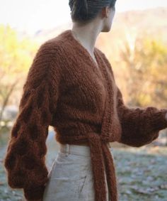 a woman wearing a brown cardigan standing in the grass with her hands on her hips