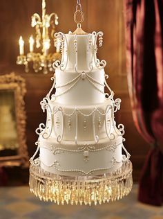 a three tiered white wedding cake sitting on top of a table next to chandelier