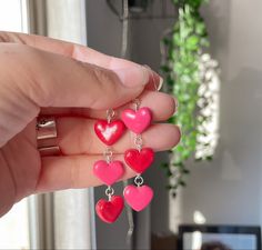 a person holding four heart shaped earrings in their hand, with the other one being held up